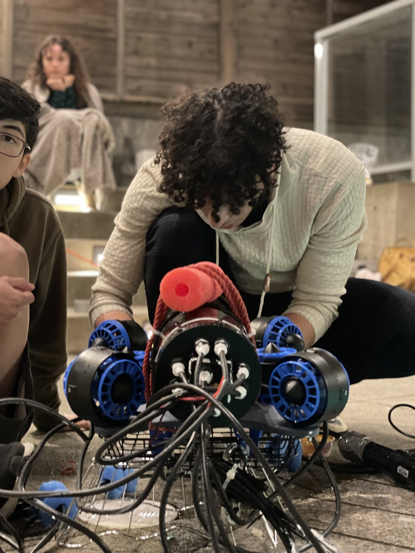 Workshop assembly of the ROV with blue thrusters and a tethered electronics enclosure